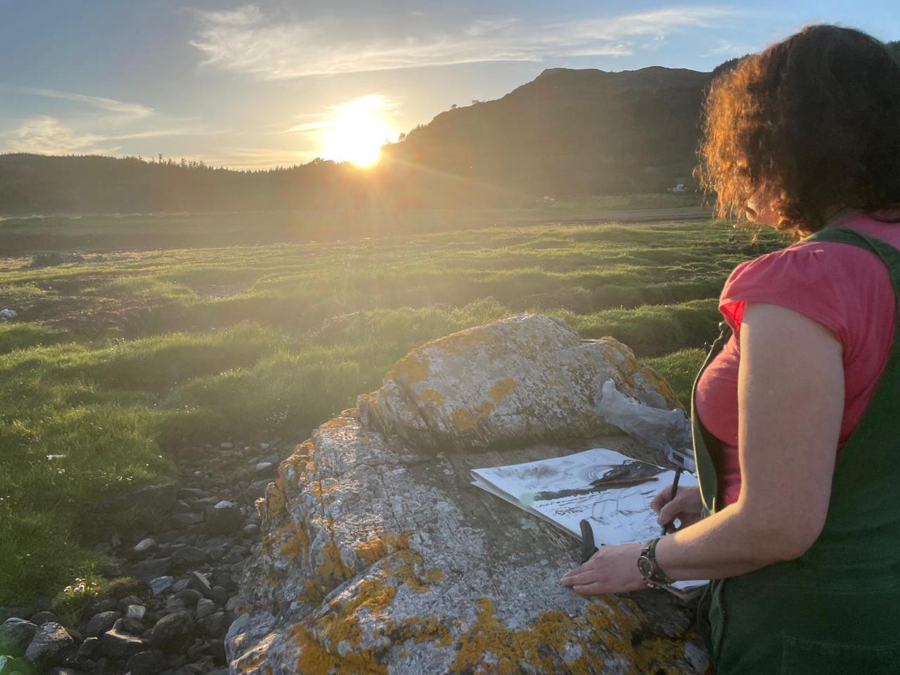 Sarah Longley drawing outdoors at sunset on the shore in Lochalsh